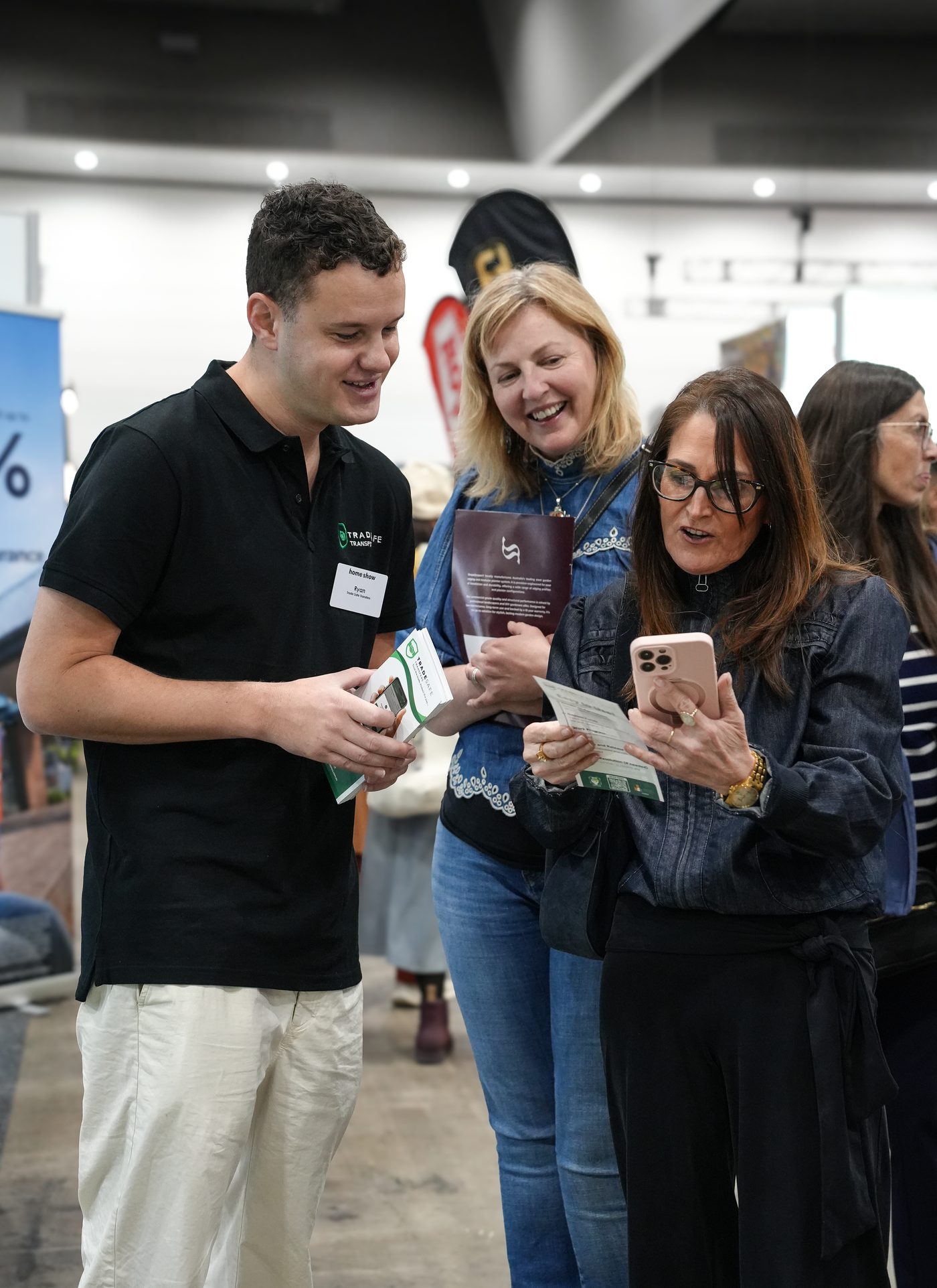 Trade Safe team member showing the app to two smiling visitors